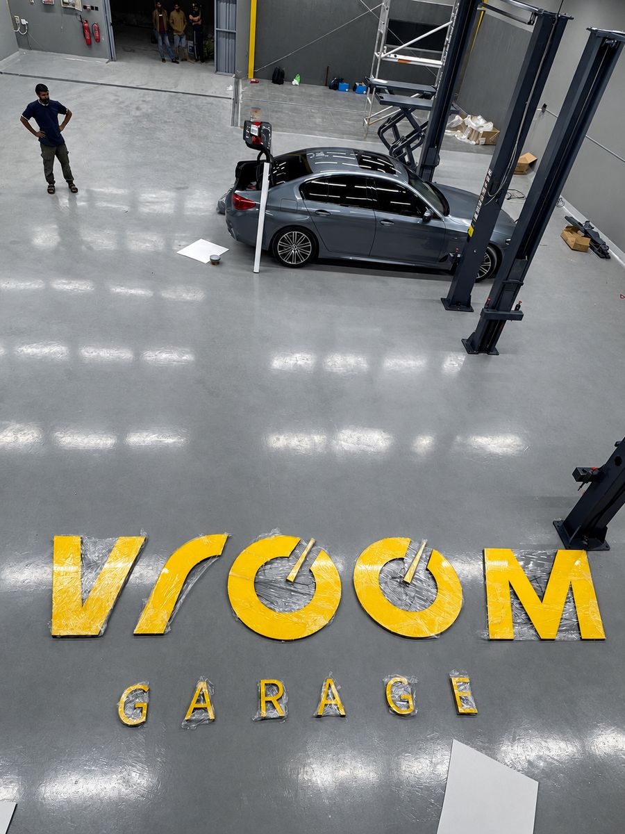 Логотип Vroom Garage, выложенный на полу гаража рядом с машиной на подъёмнике